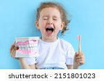 Small photo of Little cute funny smiling girl holding tooth jaw, toothbrush. Kid training oral hygiene. Child learning brushing, cleaning teeth. Prevention of caries in children. children dentistry. dental care kids