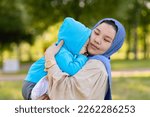 Small photo of Cute young islamic kazakh woman hugging her little crying son, newborn boy. Yappy asian mother in hijab soothes, holding baby in hands outdoors. Family concept