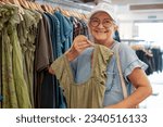 Happy senior woman looking for sale in a store selecting a green dresses enjoying shopping, consumerism sales customer shopping concept