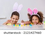 Small photo of Black girl and a boy kids smile broadly and play with Easter eggs hiding at the table at home