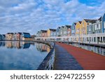 Small photo of Houten, The Netherlands - April 25 2023. Wooden bridge alongside colourful wooden lakeside houses. Reflected in the water of lake De Rietplas. Diminishing perspective.
