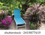 Small photo of A turquoise lounger and fuchsia petunias along with mesmerizing Purple fountain ornamental grasses in containers beckon visitors to relax on a patio on a hot summer afternoon.
