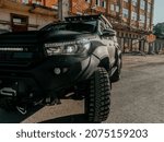 Small photo of YEKATERINBURG, RUSSIA - APRIL 30, 2020: A black Toyota Hilux against an impressive urban landscape at sunset. Wet road. Shagreen car coating. Trends in the automotive industry.
