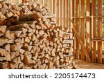 Stack of firewood. Wooden shed for storing firewood indoors. Firewood pile to be used as fuel for heating in fireplaces and furnaces. Wooden wall from pile of firewood stacked in an old farm shed. 