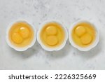 Double yolk eggs in a bowl on a white marble surface. Two yolks in one chicken egg. Identical twins. Double eggs. Flat lay