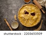 Cooking halloween apple pie, pumpkin face cutted in raw dough. Autumn baking concept, top view