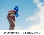 Small photo of Man Hands holding blue ribbon over blue sky, Prostate Cancer Awareness, November blue, Movember Men health awareness, world diabetes day