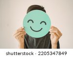 Happy mixed Asian teen boy holding smile emoji face, positive mental health concept