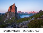 View from Mount Hesten on Iconic Mountain Segla in light of midnightsun in front of clear sky and mountain range in background, rocks and boulders in foreground, Fjordgard, Senja, Norway