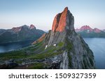 View from Mount Hesten on Iconic Mountain Segla in light of midnightsun in front of clear sky and mountain range in background, Fjordgard, Senja, Norway
