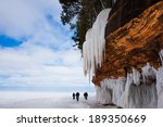 Frozen Lake Superior shoreline.  Orange cliff, large icicles, people for scale.  Copy space.  Apostle Islands National Lakeshore on Lake Superior.  Popular winter travel destination.