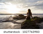 attractive woman sitting on the rocks enjoying a beautiful sunset in Playa Flamingo, Costa Rica