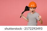 Small photo of fighting screaming boy in a gray t-shirt with a helmet on his head brandishes a big funnel and shows his fist, pink background with copy space