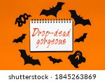 Small photo of Happy halloween holiday concept. Notepad with text Drop-dead gorgeous on white and orange background with bats, pumpkins and ghosts
