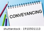 Small photo of Text Conveyancing on a white notepad with pencils on a blue background. Business concept