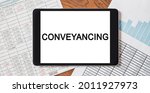 Small photo of Tablet with text Conveyancing on your desktop with documents, reports and graphs. Business and finance concept