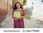 Hispanic mom with notebooks outside school in rural area - Mayan adult woman ready to go to study - Latina teacher in town