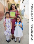 Small photo of Hispanic mom and daughters ready to go to school - Latin mom accompanying her daughters to school - Hispanic girls with backpack outside their house in rural area