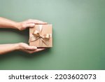 Female hands holding Christmas gift box on pastel green background.