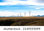 Wind turbines standing tall generating electricity with the Canadian Rocky Mountains at background near Pincher Creek Alberta Canada.