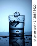Small photo of Single glass of water two ice cubes trow droplets small splash fresh cold blue light liquid reflection