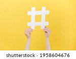 Cropped images of female hands holding large big white hashtag sign, viral web content, internet promotion, isolated on yellow studio background wall. Concept of trendy social media posts and blogging
