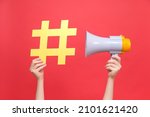 Close up female hands holding yellow hashtag sign and megaphone, label for business, marketing and advertising, isolated on red studio background. Concept social network monitoring, media measurement