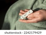 Small photo of Mans hand holding a positive Covid 19 corona antigen test while wearing a green blanket bathrobe. Home kit antigen testing and feeling ill due to sars-cov-2, a viral infection