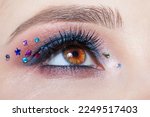 Closeup macro shot of human female brown color eye. Woman with natural evening vogue face beauty makeup. Girl with perfect skin, with blue eye shadow make up and rhinestones.