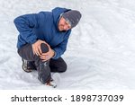 Small photo of Photo of injured young man bend down on snow and holding his knee in pain, outdoor. Young man holding his knee in pain on a snowy cold winter day. Man having a knee injury on winter road. Copy space.
