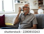 Older man having asthma attack due to his allergies. Mature man using medical inhaler to prevent and treat wheezing and shortness of breath caused by allergy.