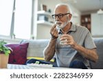 Small photo of Senior man takes pill with glass of water in hand. Stressed mature man drinking sedated antidepressant meds. Man feels depressed, taking drugs.