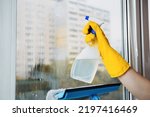 Small photo of Man in yellow gloves cleaning window with squeegee and spray detergent at home terrace. House cleaning and house chores, domestic hygiene. Window cleaning background with blue sky