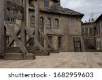 Small photo of The photo shows part of a dark medieval or pirate town with a guillotine on a wooden platform. In the background, houses with broken windows, desolation and destruction as during the plague pandemic.