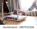 Small photo of Selective focus at router. Internet router on working table with blurred man connect the cable at the background. Fast and high speed internet connection from fiber line with LAN cable connection.