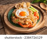 Nasi goreng- Indonesian fried rice with fried egg, chili, shrimp, kerupuk crackers in plate on wooden background. Indonesian Food