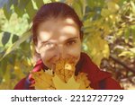 Close up portrait of positive cheerful woman cover her face with maple leaf