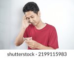 Small photo of I'm broke. Portrait of a bankrupt asian man showing his meager money. Upset crying male model standing isolated over white background wall. Poverty Concept.