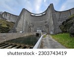 Small photo of An impressive dam on a river in France showing the water supply channel and the dam wall during the dry season with blue sky above and green grass and rocks to either side