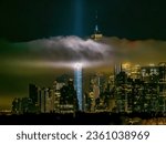 Aerial view of low lying clouds positioned in front of the Freedom Tower in New York City at night, while the tribute in light beams are illuminated.