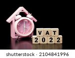 Small photo of Vat Concept. Vat 2022 word is written on wood block and clock on black background.