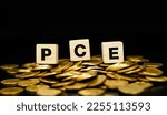 Small photo of Text "PCE" (Personal Consumption Expenditure) on wooden cube with stacks of gold coins. economic data concept.