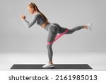 Athletic girl doing exercise for glutes with resistance band on gray background. Fitness woman working out