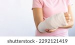 Small photo of Close-up of a woman's broken arm in a cast. The girl holds a bent arm against the background of a pink t-shirt. Banner, copy space. Insurance medicine concept.