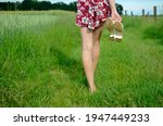 Barefoot girl walking on green grass. Slim girl holding her shoes in hand, wearing colorful skirt. Summer in Poland, beautiful farmland in Lower Silesia.