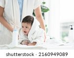 Small photo of Cute Caucasian little toddler baby girl wear bathrobe after bathing is smiling and lying on towel while mother wipe and apply talcum powder on her body. Hygiene care for children concept