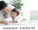 Small photo of Cute Caucasian little toddler baby girl wear bathrobe after bathing is smiling and lying on towel while mother wipe and apply talcum powder on her body at home. Hygiene care for children concept