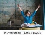 Happy hipster student rejoicing in success of training project holding hands up.Overjoyed young woman completed studying task during exam preparation sitting at desktop with laptop and textbook