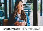 Small photo of Attractive female blogger with modern smartphone gadget in hands thoughtful looking away and dreaming, youthful Caucasian blogger holding cellphone pondering thinking on idea for social publication