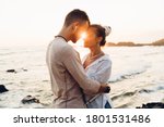Small photo of Side view of amorous man and woman in elegant clothes embracing each other while standing near waving sea on beach